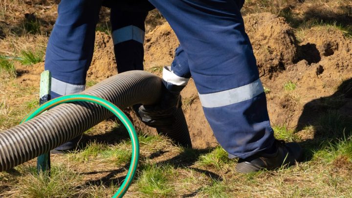Worker holding suction hose at an open manhole beside pumping machine