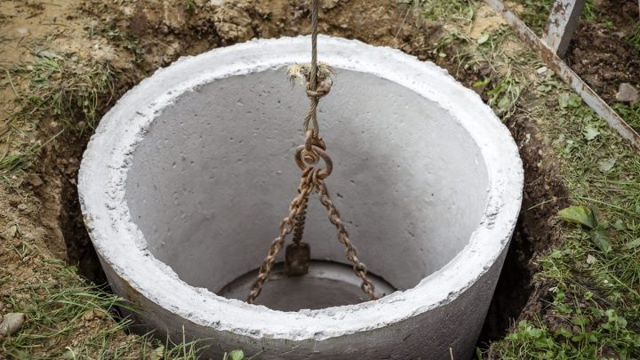 Concrete septic ring being lowered into an open excavation beside a house