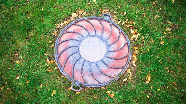 Round sewer access hatch sitting flush in a mown lawn