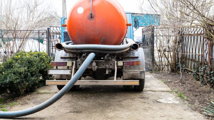 Sewage pump truck tank and hose emptying a septic tank