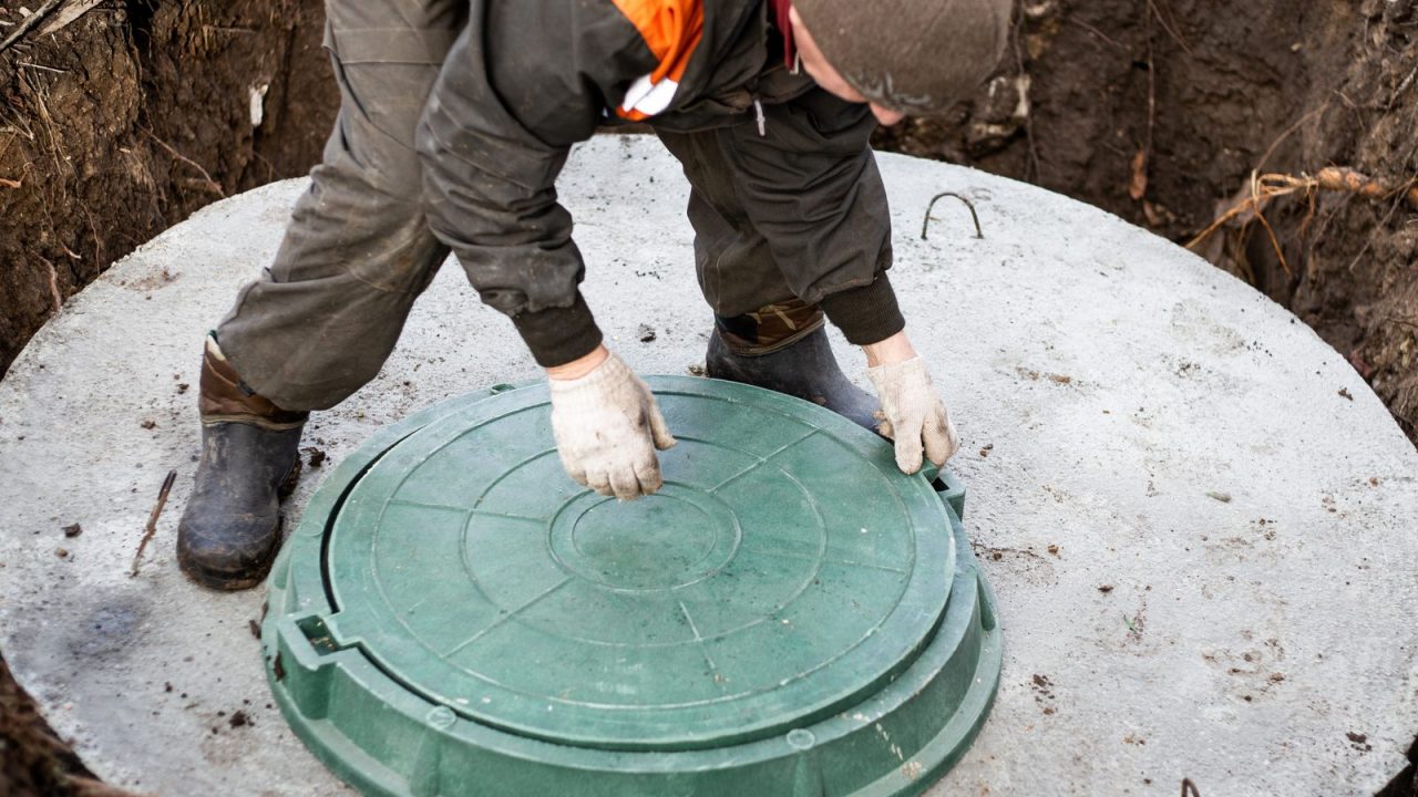 Worker closing the manhole lid on a septic well at a rural house