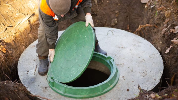 Worker fitting a sewer manhole onto a septic tank built from concrete rings