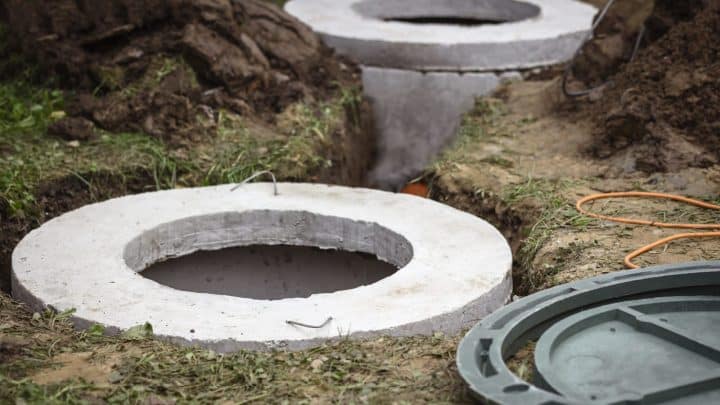 Two concrete sewage wells with manhole covers set in excavated ground