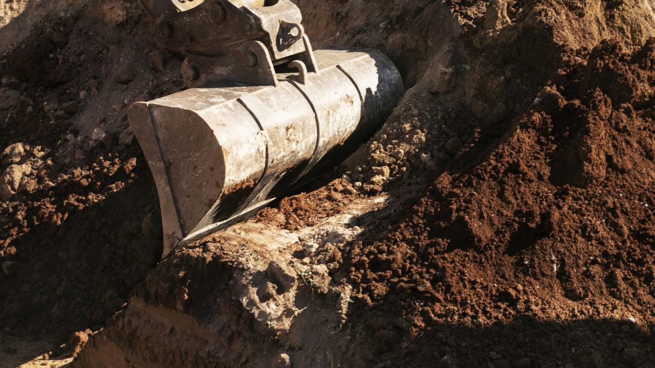 Excavator bucket digging soil, open ground