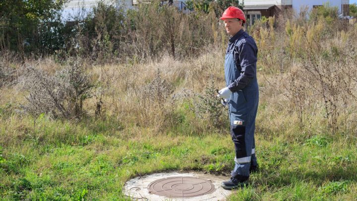 Worker standing at an open underground chamber in a rural yard