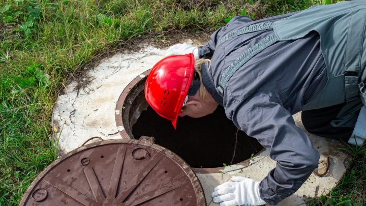 Plumber lifting an underground chamber lid to inspect inside