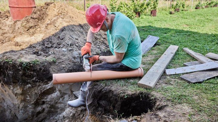 Worker cutting a plastic sewer pipe with an angle grinder